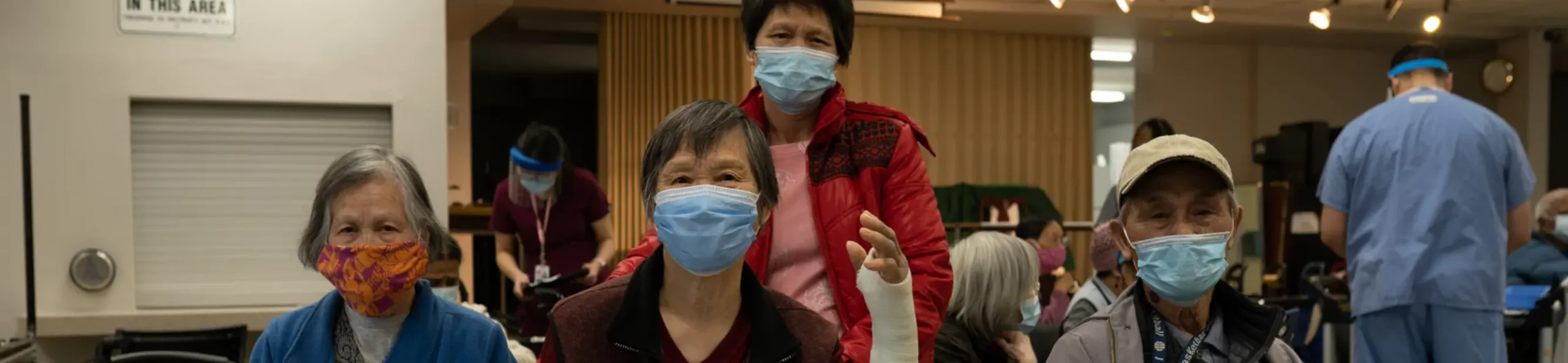 A photo of tenants and healthcare workers, all wearing masks. Two of the tenants are looking directly at the camera. One has a broken arm.